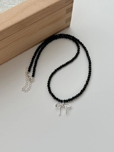 Gros plan du pendentif nœud en argent S925 et perles noires sur collier minimaliste