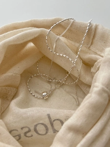 Detailed macro view of S925 silver cylinder pendant necklace inside a linen pouch