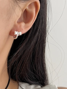 Close-up of a silver bow earring on model's ear, showing the delicate metallic luster