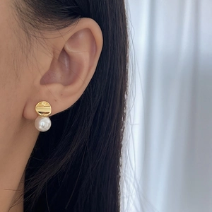 Elegant white pearl drop earrings with gold disc studs worn on model's ear