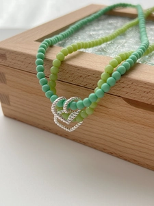 Detail of silver hollow heart pendant on green and yellow beaded double necklace