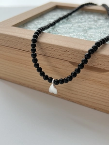 Detail of black onyx beaded necklace featuring a silver heart pendant on a wooden jewelry box