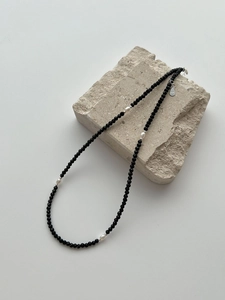 Macro detail of S925 sterling silver tag on a black beaded necklace with baroque pearls