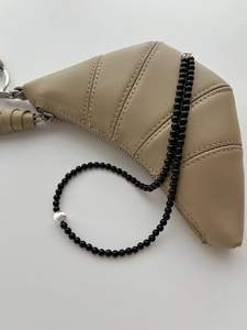 Détail d'un collier en agate noire avec perle en argent brossé sur sac en cuir beige