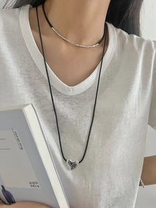 Close-up of layered silver heart pendant and black beaded necklace on model