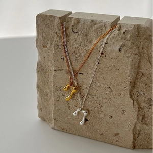 Modern minimalist gold and silver molten metal teardrop pendant necklaces on stone