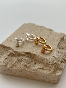 Detailed view of gold and silver bow hoop earrings on a textured stone surface