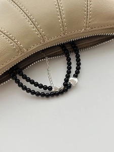 Détail du collier de perles en onyx argent s925 dans un sac en cuir beige