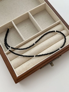 Detailed close-up of black spinel beaded necklace with silver spacers in wooden box