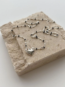 Close-up of S925 silver heart necklace with black beads on a textured stone surface
