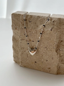 Detailed close-up of S925 silver heart necklace with black beads on stone prop
