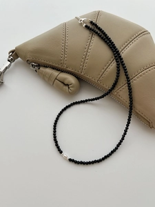 Macro view of dainty black spinel beaded necklace with a natural freshwater pearl on beige leather