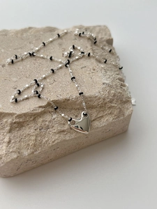 Close-up of silver heart pendant with black beaded chain on a natural stone prop