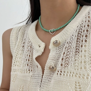 Mint green beaded necklace with interlocking heart pendants on a cream knit vest
