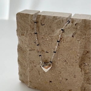 Polished silver heart pendant necklace with black beads on a natural stone display