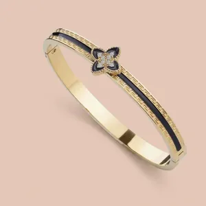 Gold-plated cuff bracelet featuring black enamel, clover charm, and Greek key patterns
