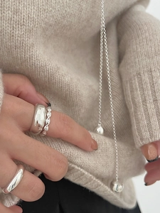 Close-up of three 925 sterling silver rings and a beaded chain on a beige sweater