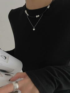 Detail of layered silver heart pendant necklace and pearl beads on a black outfit
