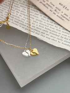 Detailed view of gold and silver heart puzzle necklaces with keyhole design on vintage paper