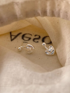 Détail de boucles d'oreilles cœur argentées avec finition miroir dans un pochon en lin