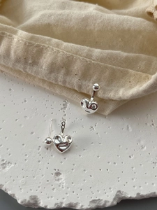 Gros plan de boucles d'oreilles cœur en argent 925 avec clous boule sur du lin