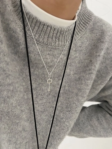 Detailed view of a silver key pendant necklace worn on a textured grey knit sweater
