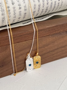 Macro detail of gold and silver rectangular sunburst necklaces with blue evil eye stones