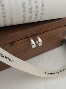 Détail macro de boucles d'oreilles créoles tressées argentées sur une boîte à bijoux