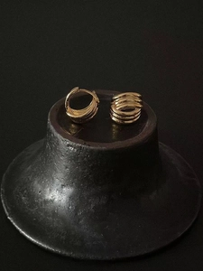 Vue macro de boucles d'oreilles créoles dorées à trois couches sur un support minimaliste