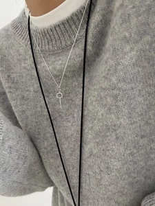 Close-up of minimalist S925 sterling silver key pendant on a fine chain worn over a sweater