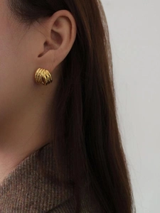 Gros plan de boucles d'oreilles dorées géométriques avec texture nervurée sur l'oreille