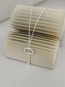 Detail of a minimalist silver key pendant necklace hanging from an open book