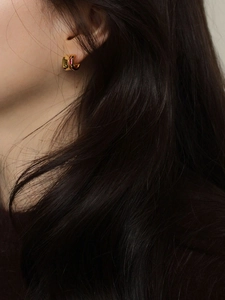 Close-up of a gold huggie hoop earring with a square pink gemstone worn on the ear
