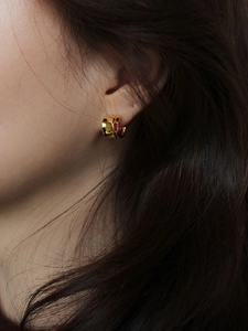 Close-up of gold hoop earrings with a rectangular red gemstone on female model