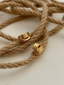 Gros plan de boucles d'oreilles géométriques dorées à spirales sur un support en corde de chanvre