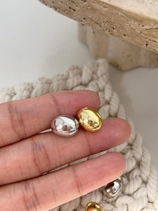 Detailed macro view of minimalist polished metallic bean earrings in gold and silver