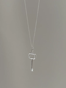 Close-up of minimalist S925 silver key pendant with fine curb chain on neutral background