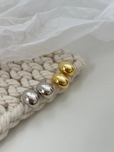 Detail view of minimalist gold and silver pebble earrings on a cozy knit background