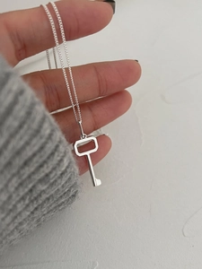 Close-up of minimalist silver key pendant necklace worn against a clean white backdrop