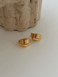 Détail des boucles d'oreilles créoles dorées torsadées multicouches sur un socle en pierre