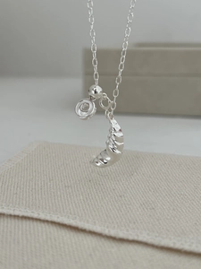 Detailed close-up of a silver croissant pendant necklace on a soft beige fabric background