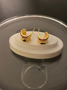 Close-up of gold semi-hoop earrings with rectangular pink crystals on white display