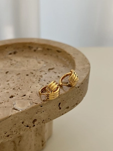Détail macro de boucles d'oreilles dorées ondulées avec finition polie sur socle en pierre