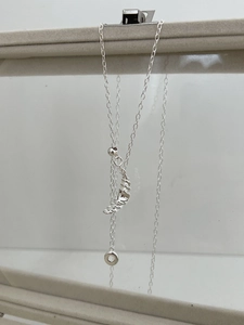 Detail view of a silver croissant pendant with a delicate link chain on a display stand