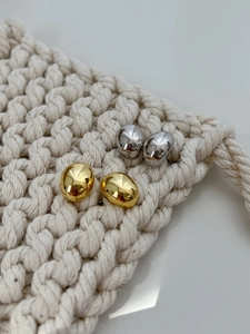 Detail of gold and silver bean stud earrings on a textured knit fabric background