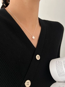 Close-up of matte silver oval pendant necklace worn on a black knit sweater for women