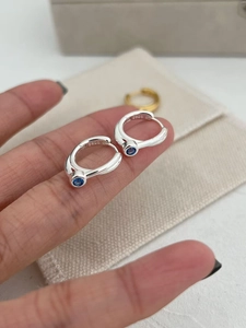 Close-up of S925 sterling silver hoop earrings with round blue zircon held in hand