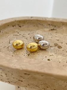 Detailed view of polished gold and silver metal bean earrings on a beige stone tray