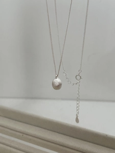 Detail shot of a minimalist S925 sterling silver necklace featuring a brushed ball pendant