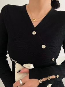 Detail of delicate gold ribbon bow necklace worn with a black v-neck ribbed knit sweater